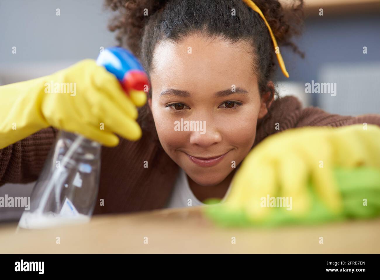 Sorry Keime, Sie haben das falsche Haus gewählt. Eine Frau trägt Handschuhe und hält eine Sprühflasche, während sie zu Hause eine Holzfläche reinigt. Stockfoto