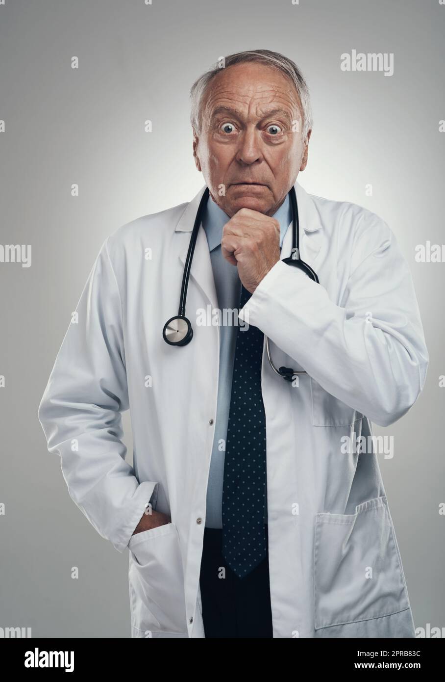 Das ist eine ziemlich schockierende Entwicklung. Ein älterer männlicher Arzt in einem Studio vor grauem Hintergrund. Stockfoto