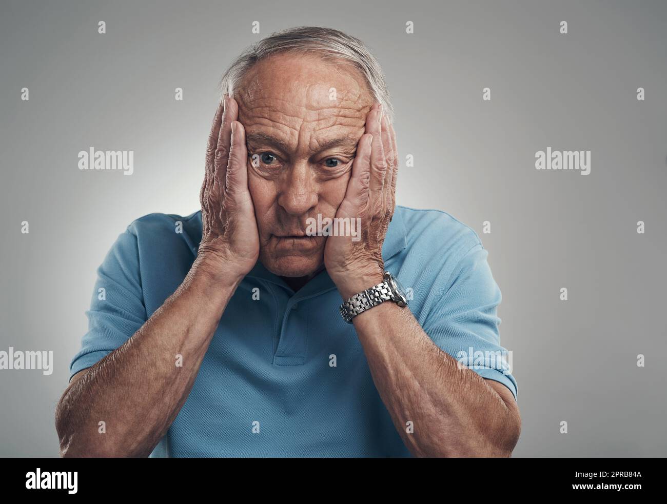 Dieser Tag war so herausfordernd: Ein älterer Mann klatschte sich in einem Studio vor grauem Hintergrund die Hände ins Gesicht. Stockfoto