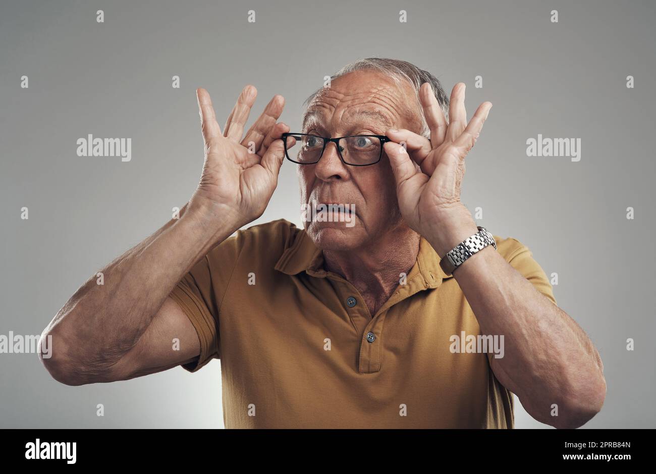 Wie meine neuen Spezifikationen. Studioaufnahme eines älteren Mannes, der seine Brille vor einem grauen Hintergrund anpasst. Stockfoto