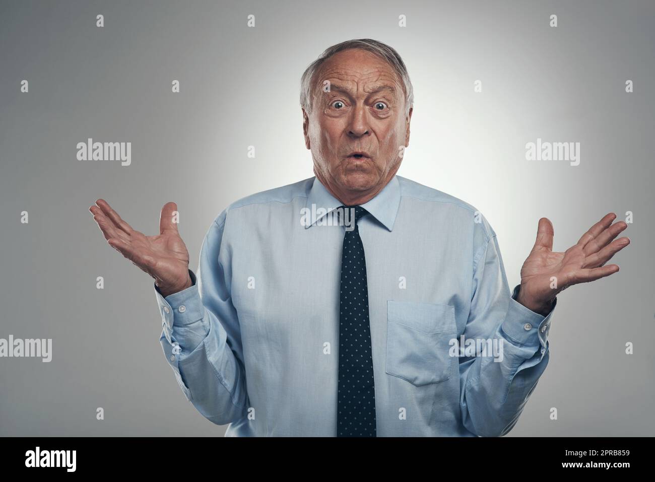 Was versuchst du mir zu sagen: Ein älterer Geschäftsmann, der allein vor grauem Hintergrund im Studio steht und verwirrt aussieht. Stockfoto