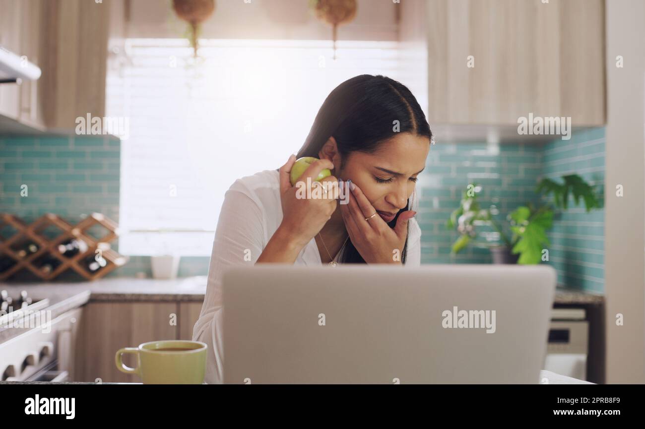 Ich muss zu hart gebissen haben: Eine junge Geschäftsfrau, die unter Zahnschmerzen leidet, während sie zu Hause einen Apfel isst. Stockfoto