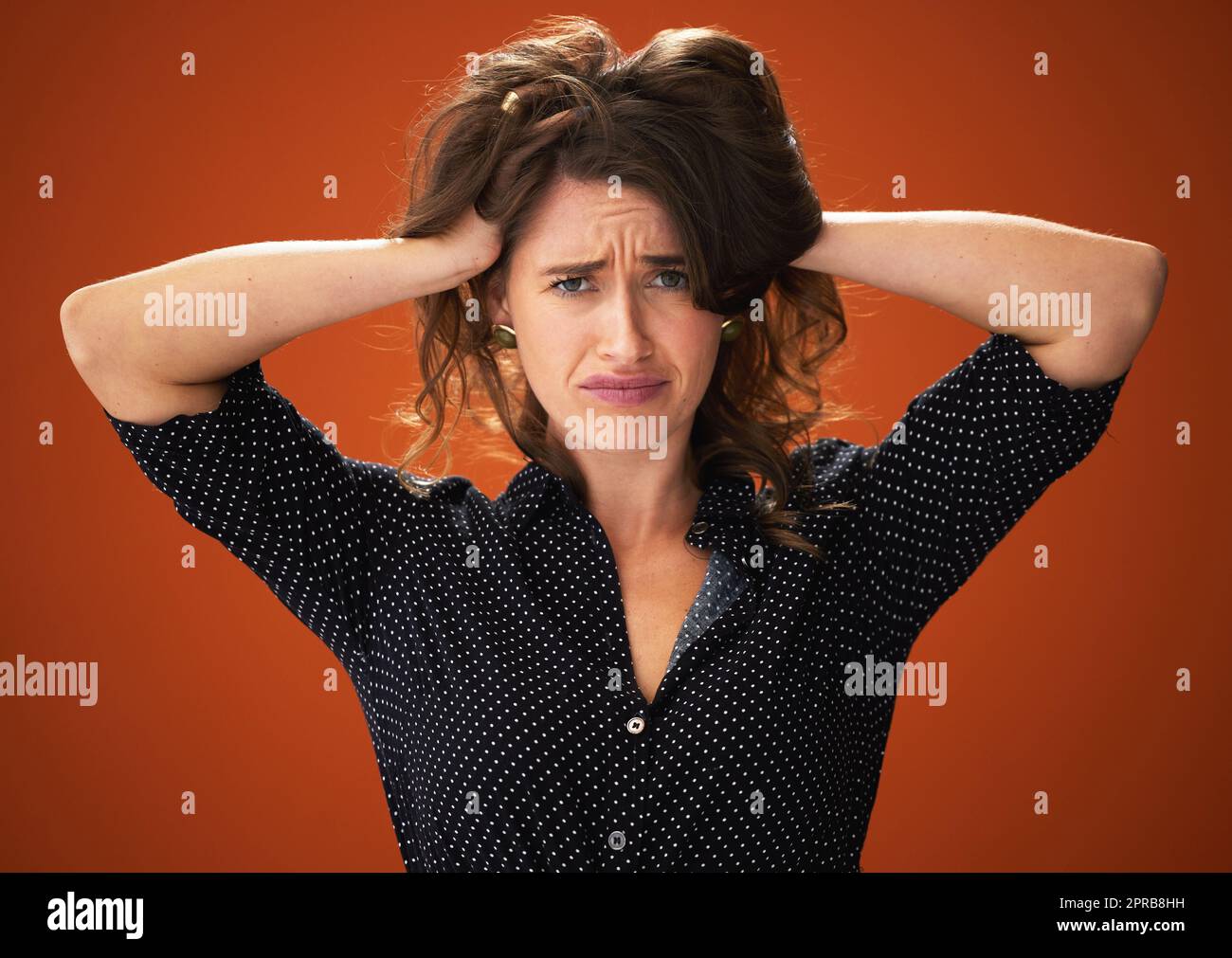 Schicken Sie Hilfe. Eine attraktive junge Frau, die allein vor rotem Hintergrund im Studio steht und ihr Haar berührt. Stockfoto