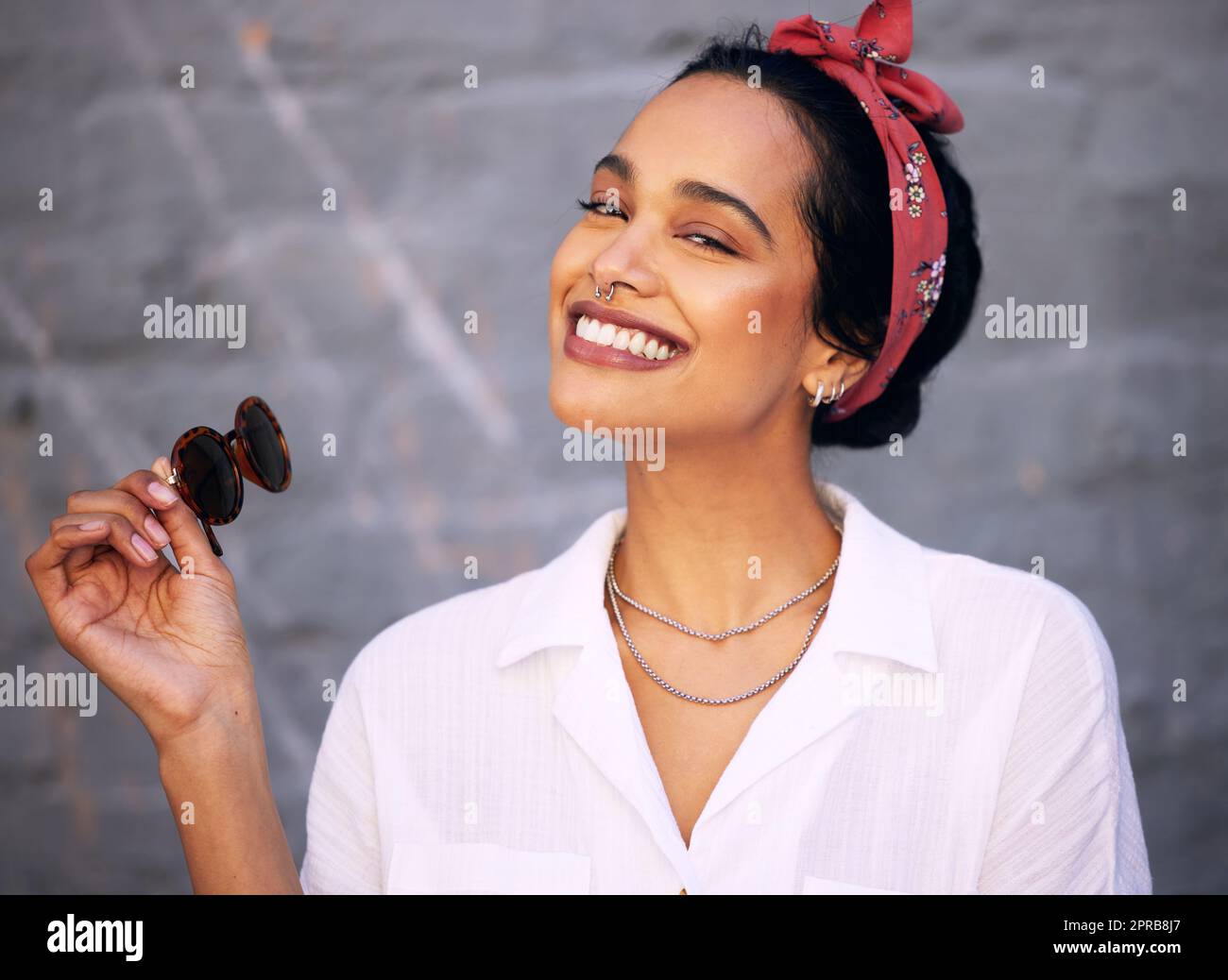 Ein Lächeln ist ansteckend: Eine attraktive junge Frau, die allein an einer grauen Wand steht und tagsüber posiert. Stockfoto