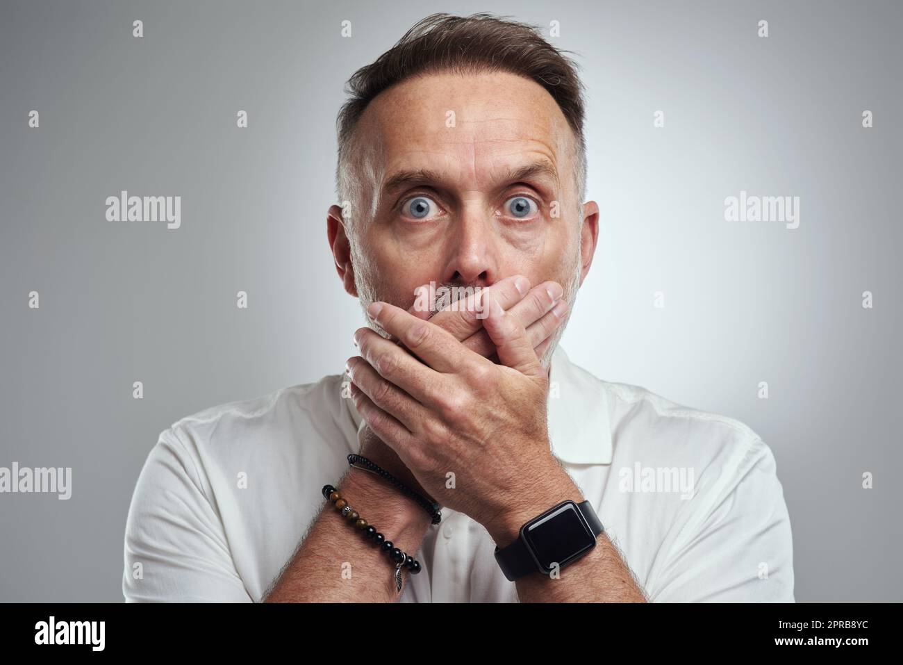 Hoppla, das sollte ich Ihnen eigentlich nicht sagen. Studioporträt eines reifen Mannes, der seinen Mund bedeckt und schockiert vor grauem Hintergrund aussieht. Stockfoto