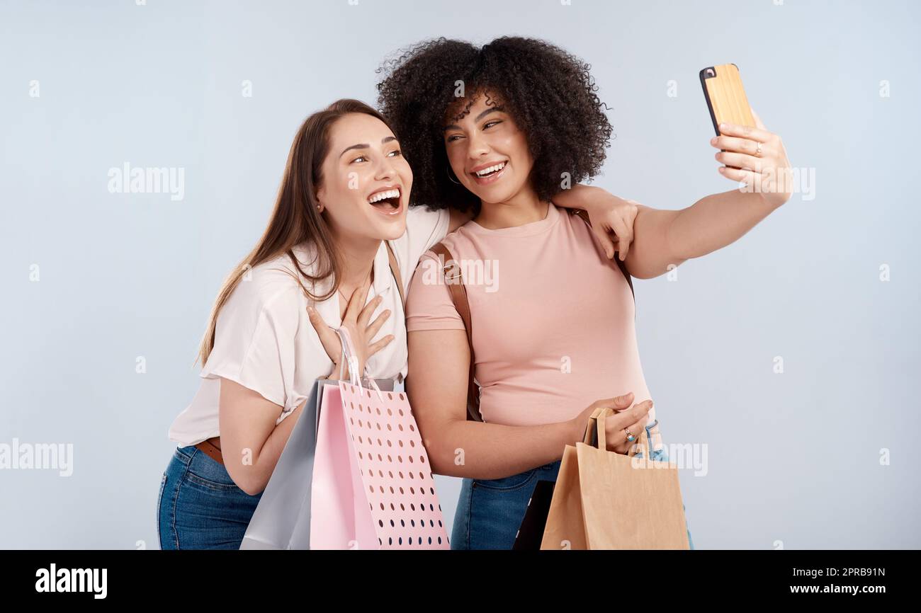 Bargainbuddys. Studioaufnahme von zwei jungen Frauen, die eine Reihe von Einkaufstaschen tragen und ein Selfie machen. Stockfoto