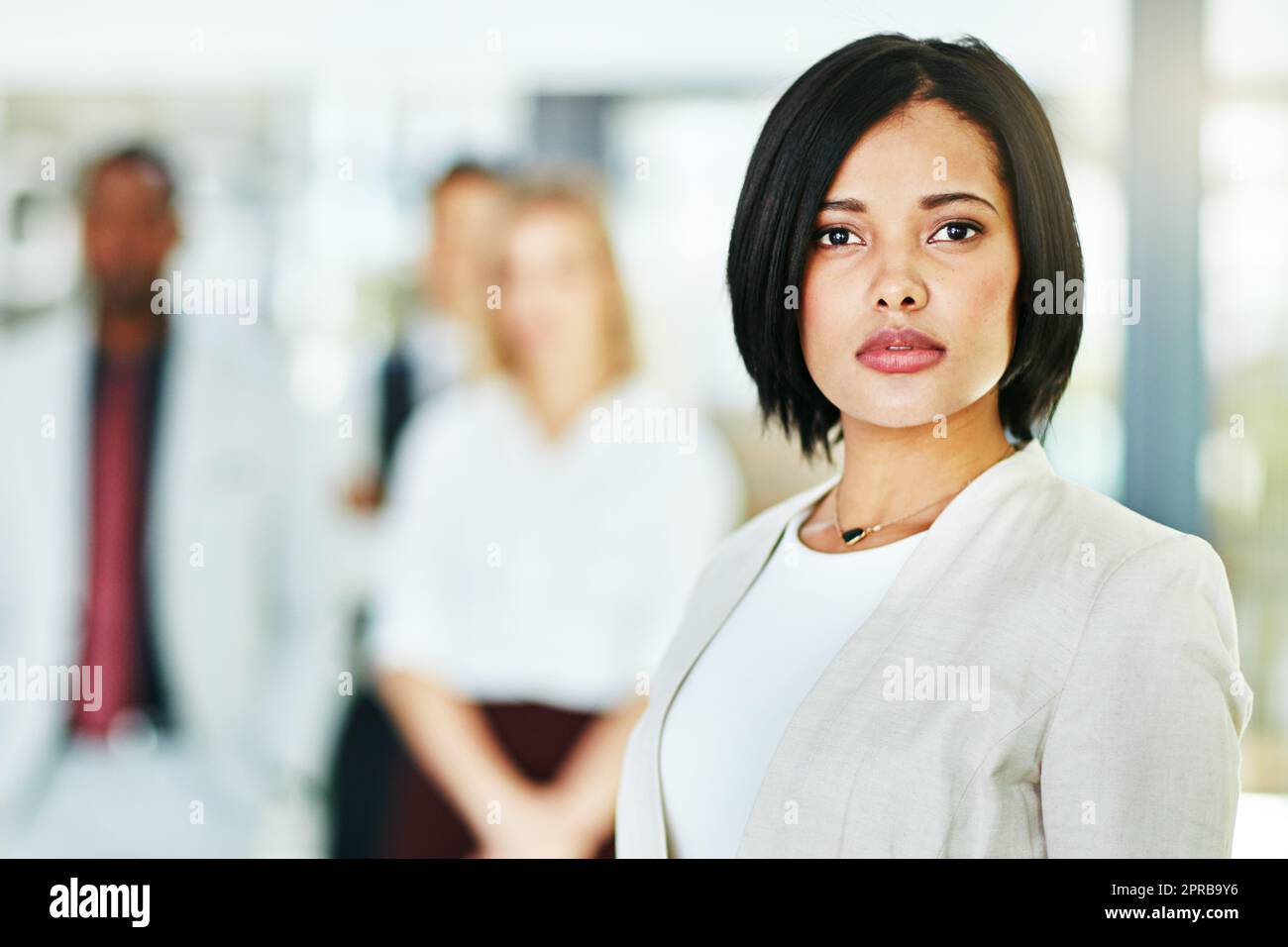 Seriöse, fokussierte und selbstbewusste Anwältin, die in die Kamera schaut und mit ihrem Team in ihrem Büro steht. Porträt eines Führers, klugen und intelligenten Anwalts, der hart und belastbar ist Stockfoto