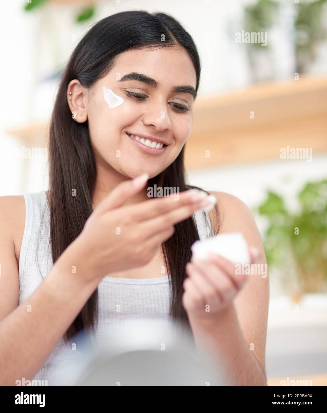 Hydratisieren Sie Ihren Weg zu einer gesunden, prallen Haut. Eine schöne junge Frau, die ihre Feuchtigkeitscreme ansieht. Stockfoto