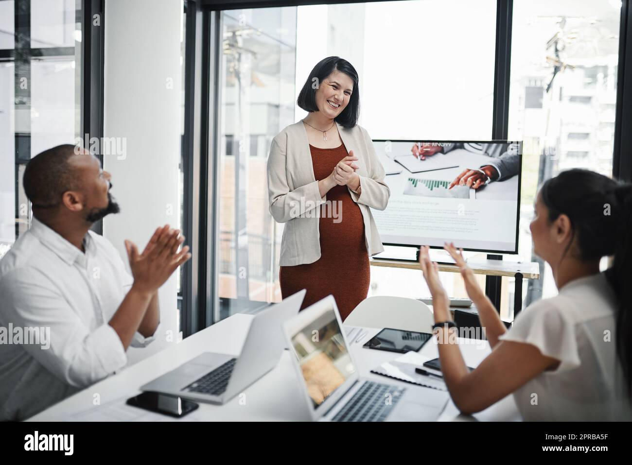 Wachstum erfordert eine gesunde Portion Ermutigung. Eine Gruppe von Geschäftsleuten klatscht während eines Treffens mit ihrer Schwangeren Kollegin in einem modernen Büro. Stockfoto