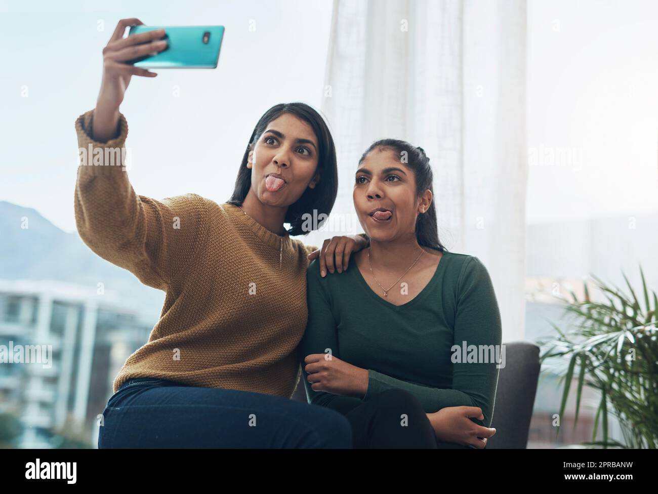 Dumme Selfies mit meiner Schwester. Zwei junge Frauen, die zusammen ein Selfie machen, während sie zu Hause sitzen. Stockfoto