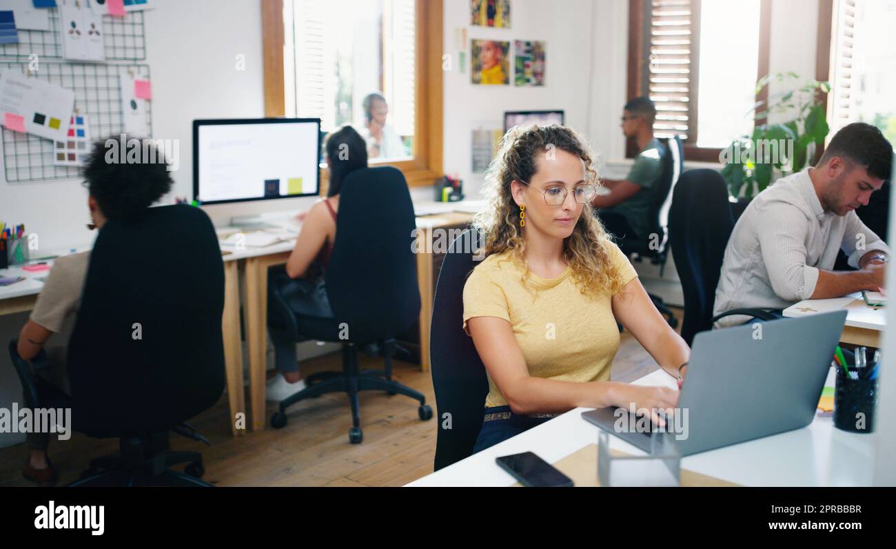 Wenn es um harte Arbeit geht, hält sie sich nicht zurück: Eine junge Geschäftsfrau, die in einem modernen Büro einen Laptop benutzt. Stockfoto