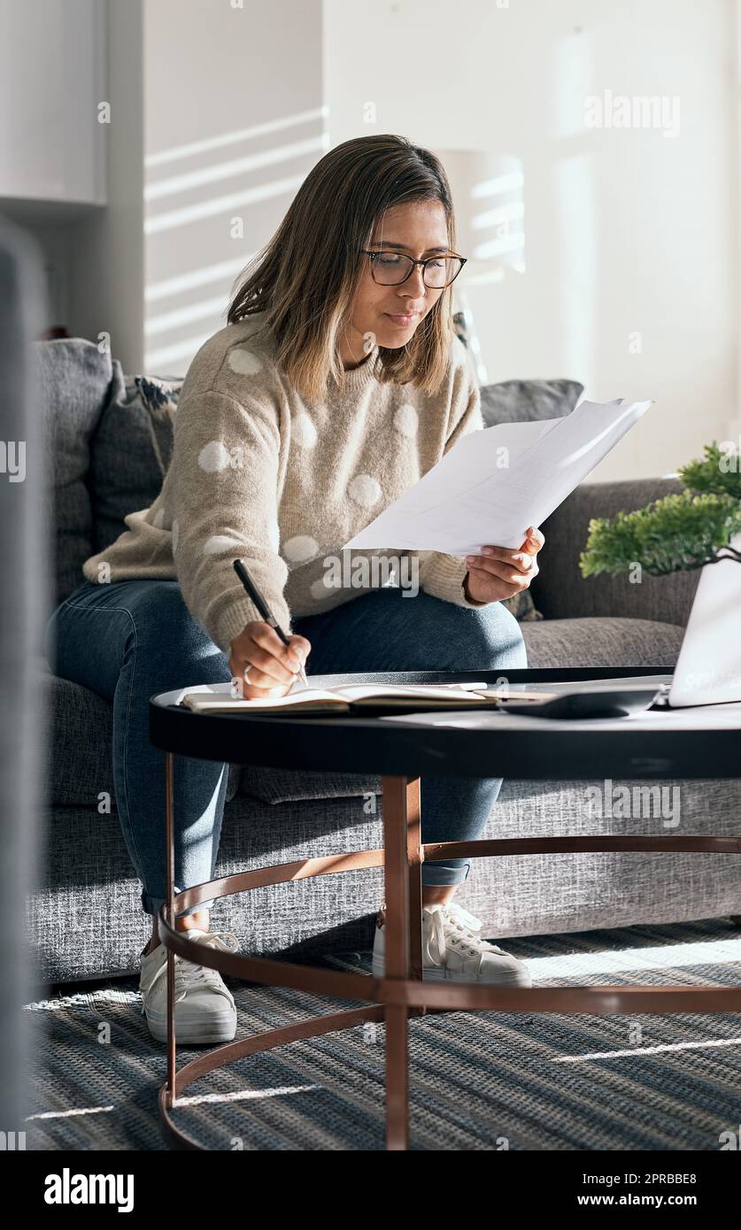 Ich schätze die Flexibilität und den Komfort, den Fernarbeit bietet. Eine junge Frau, die sich Papierkram ansieht, während sie von zu Hause aus arbeitet. Stockfoto