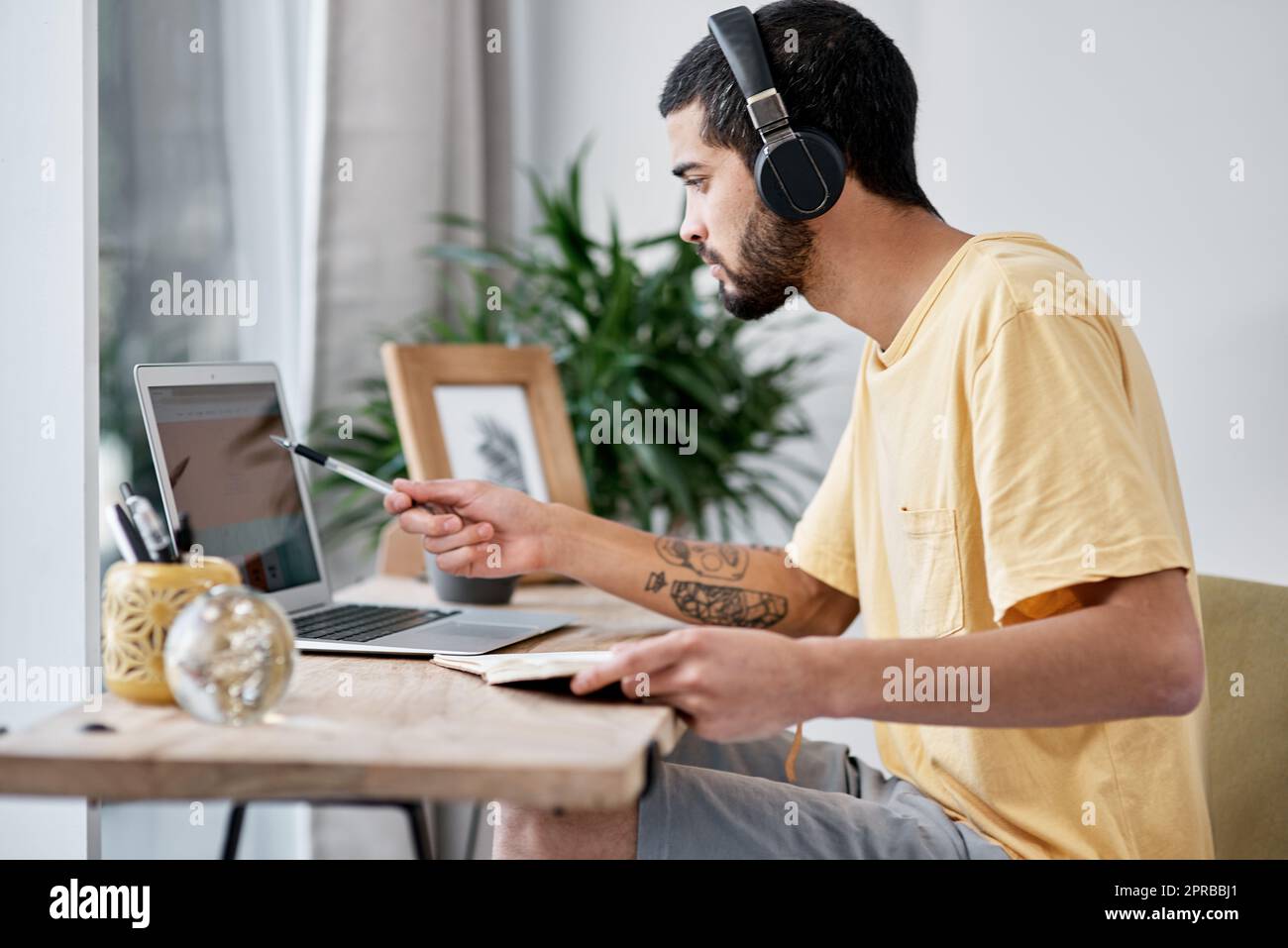 Ein junger Mann, der von zu Hause aus mit einem Laptop und Kopfhörern arbeitet. Stockfoto