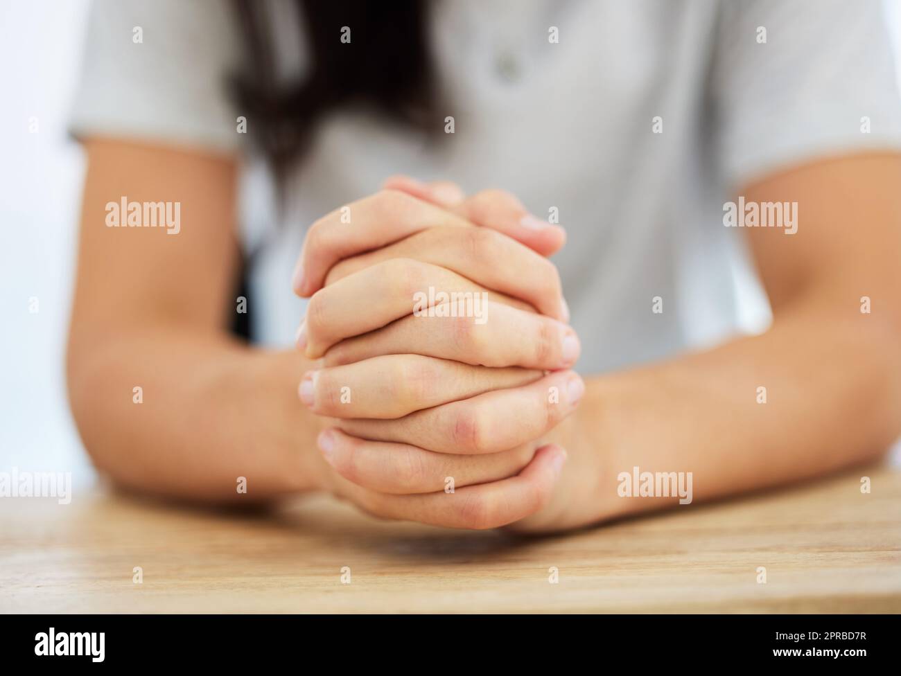 Immer den Glauben bewahren. Eine anonyme Frau, die an einem Tisch sitzt und ihre Hände zusammengeklemmt hat. Stockfoto