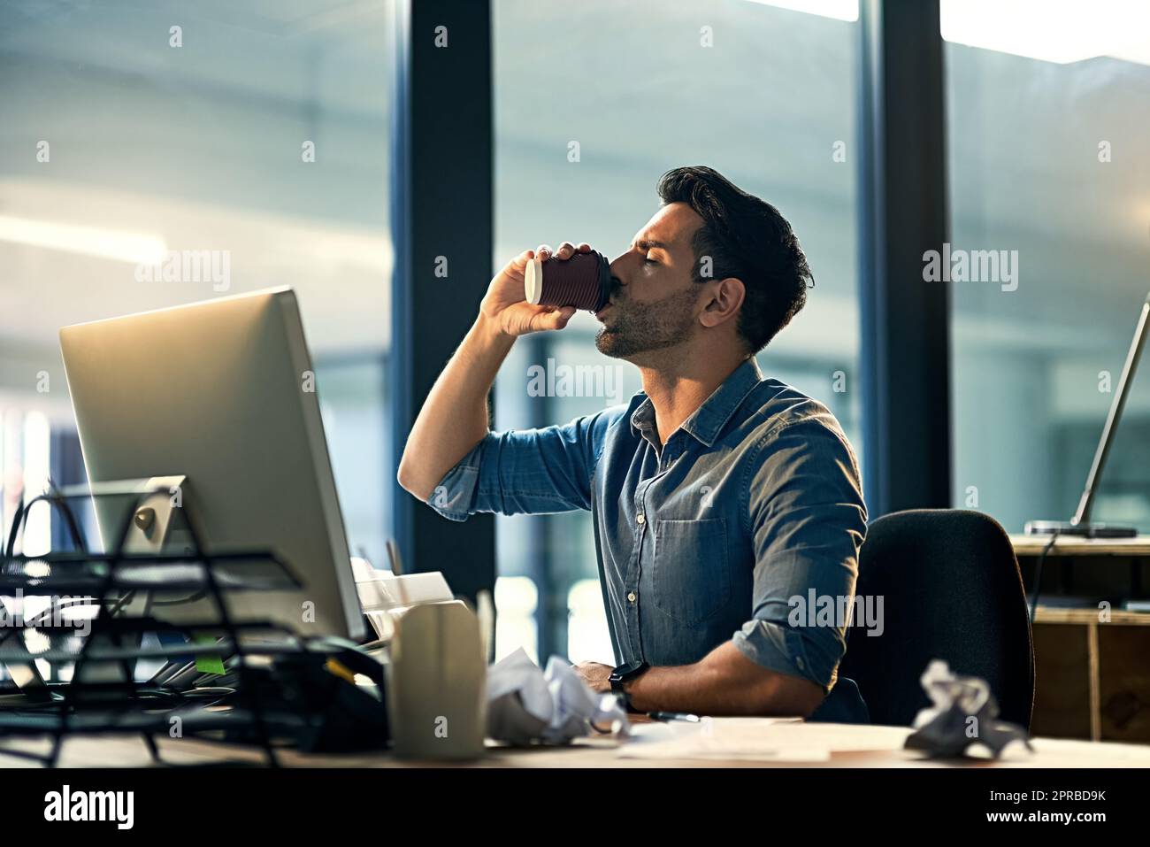 Wach bleiben bei der Arbeit mit einem Koffeinschub. Aufnahme eines jungen Geschäftsmannes, der während einer späten Nacht auf der Arbeit Kaffee trinkt. Stockfoto