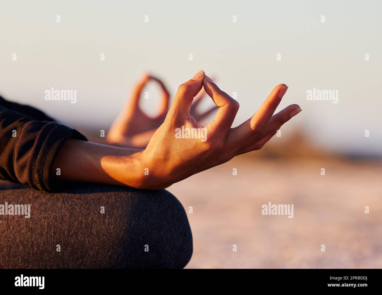 Balancieren meiner Chakren durch Meditation. Eine unkenntliche Frau sitzt allein und meditiert am Strand bei Sonnenuntergang. Stockfoto