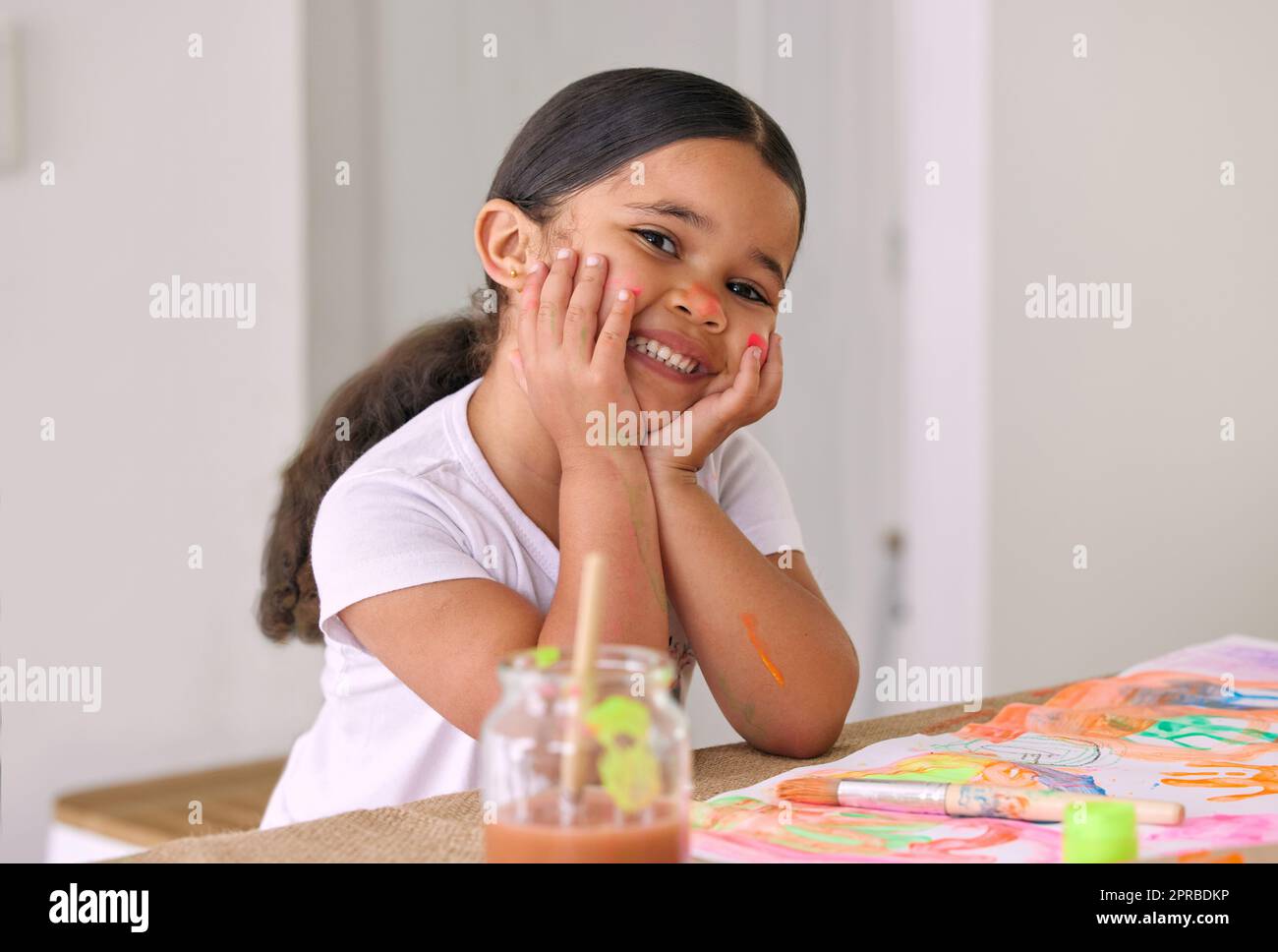 Malerei ist eine große Spielaktivität für Kinder jeden Alters. Ein entzückendes kleines Mädchen malen, während an einem Tisch sitzen. Stockfoto