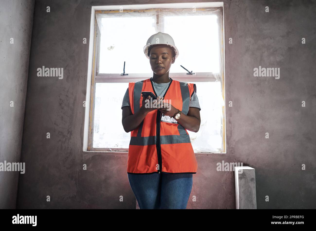 Eine junge Frau, die auf einer Baustelle mit einem Smartphone arbeitet. Stockfoto