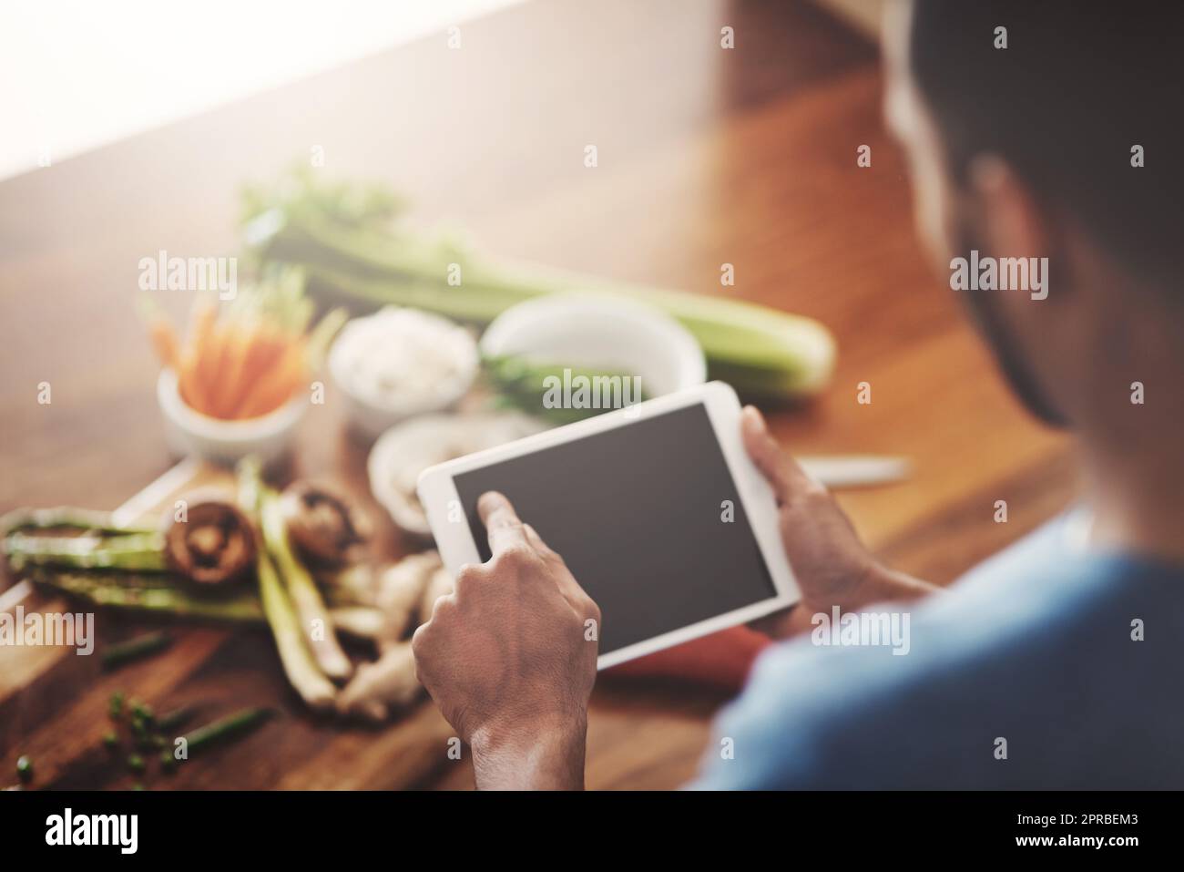 Nahaufnahme von Händen eines Mannes, der ein Tablet hält, um ein Rezept zu durchsuchen, Recherchen zu betreiben oder nach Zutaten zu suchen, während er Abendessen, Mittagessen oder Frühstück kocht. Scrollen Sie online, durchsuchen Sie die App und suchen Sie nach Essensideen Stockfoto