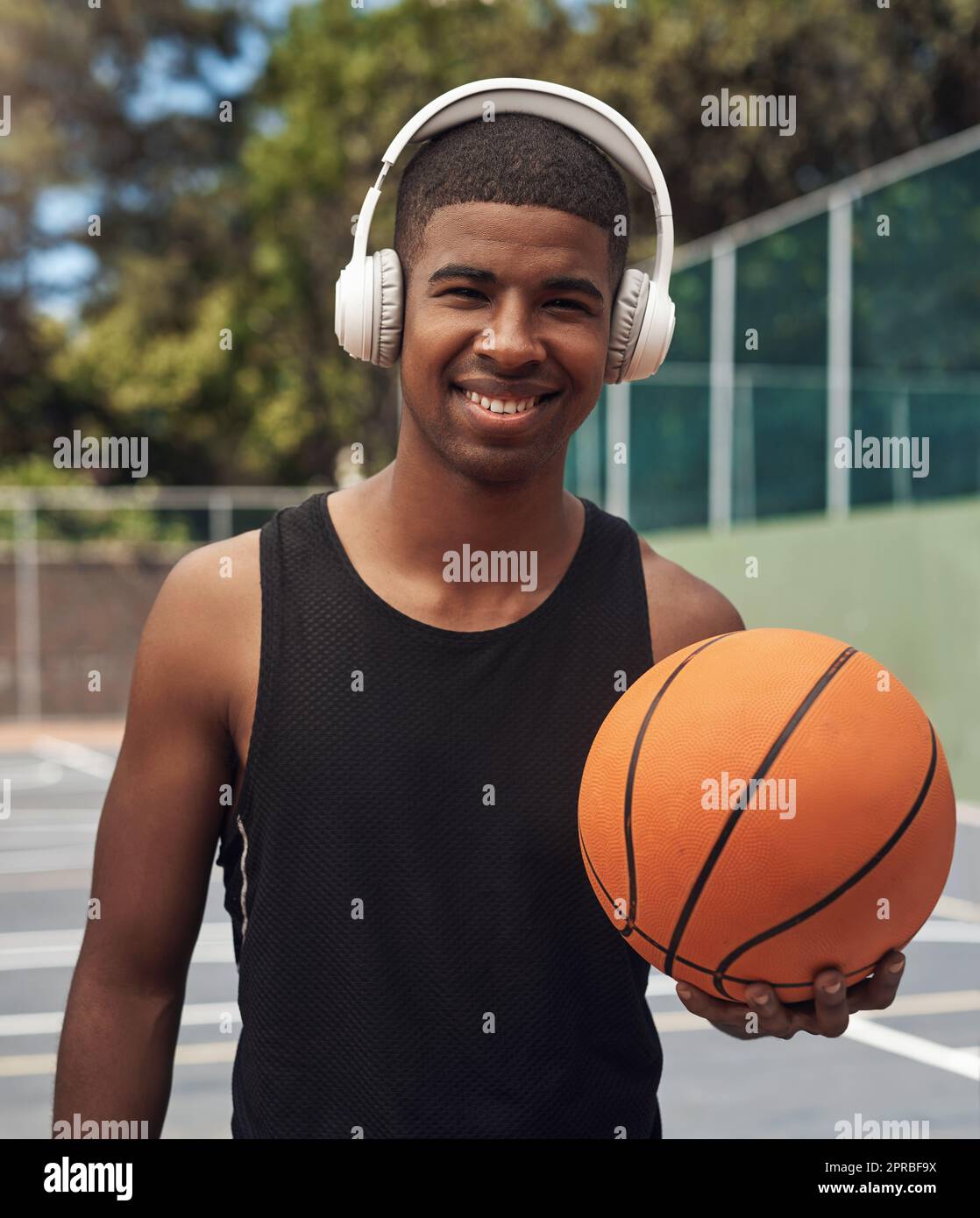 Spielen Sie mit ganzem Herzen. Porträt eines sportlichen jungen Mannes, der Musik hört, während er auf einem Sportplatz Basketball spielt. Stockfoto