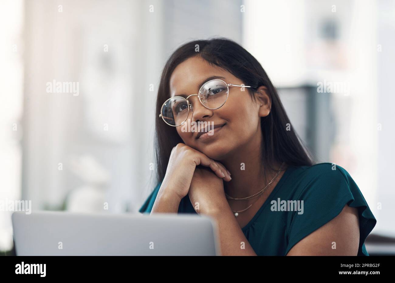 So viele klugen Ideen kommen ihr in den Sinn. Eine junge Geschäftsfrau, die nachdenklich aussieht, während sie in einem Büro an einem Laptop arbeitet. Stockfoto