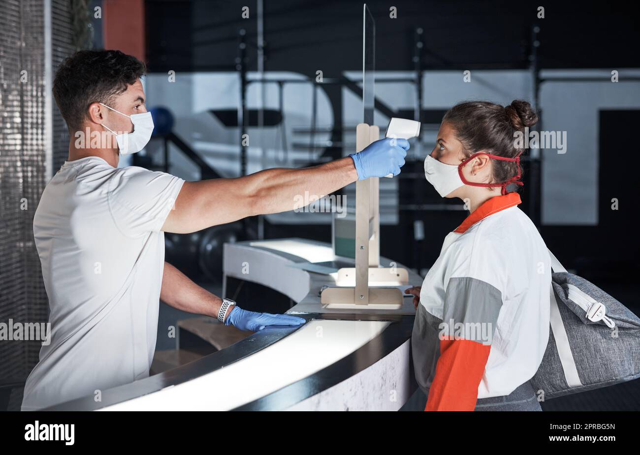 Eine junge Frau, die ihre Temperatur mit einem Infrarot-Thermometer in einer Turnhalle gemessen bekommt. Stockfoto