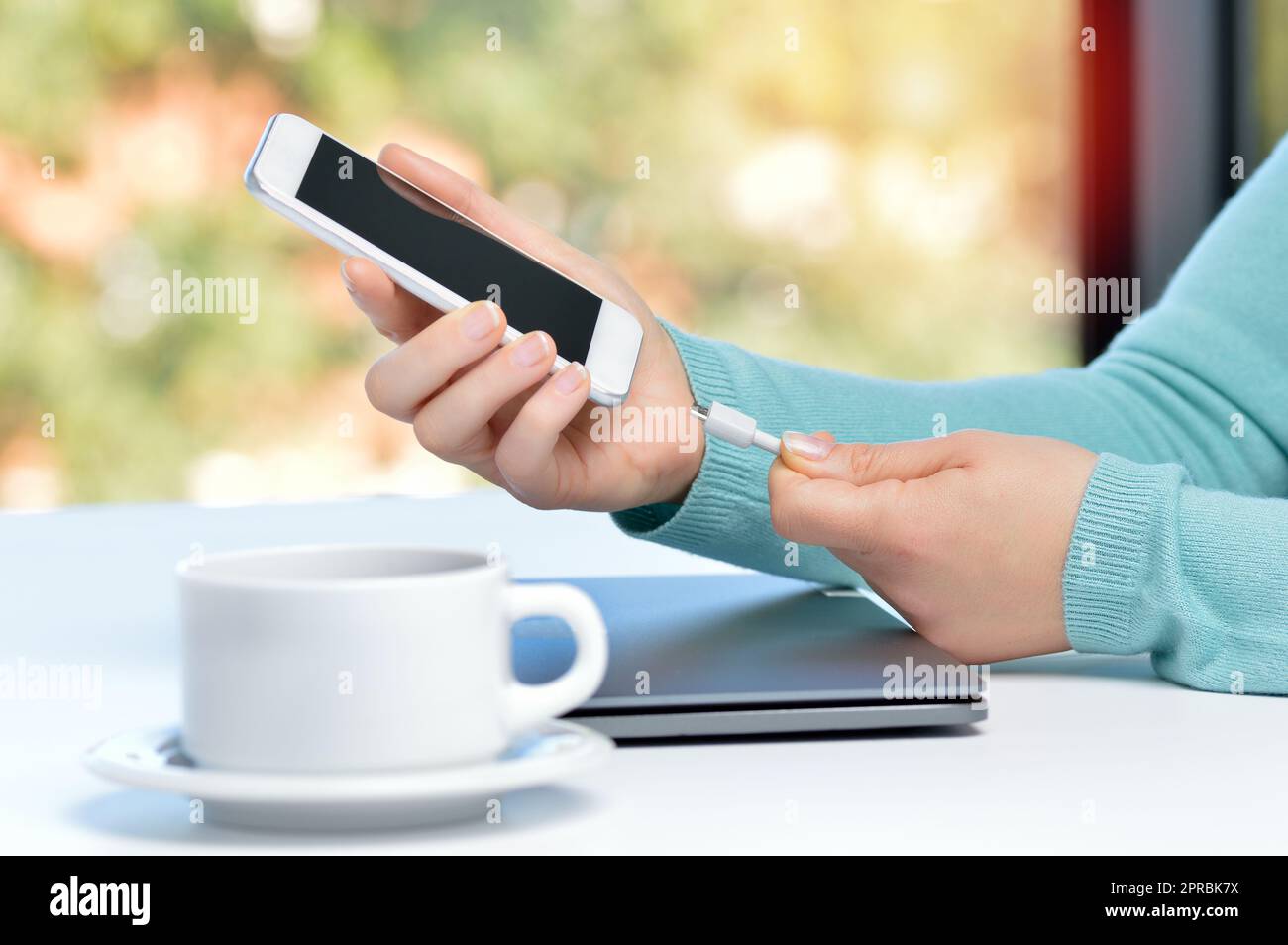 Mädchen Hand Smartphone in einer Tabelle zu Hause mit einem Fenster im Hintergrund Ladegerät anschließen Stockfoto