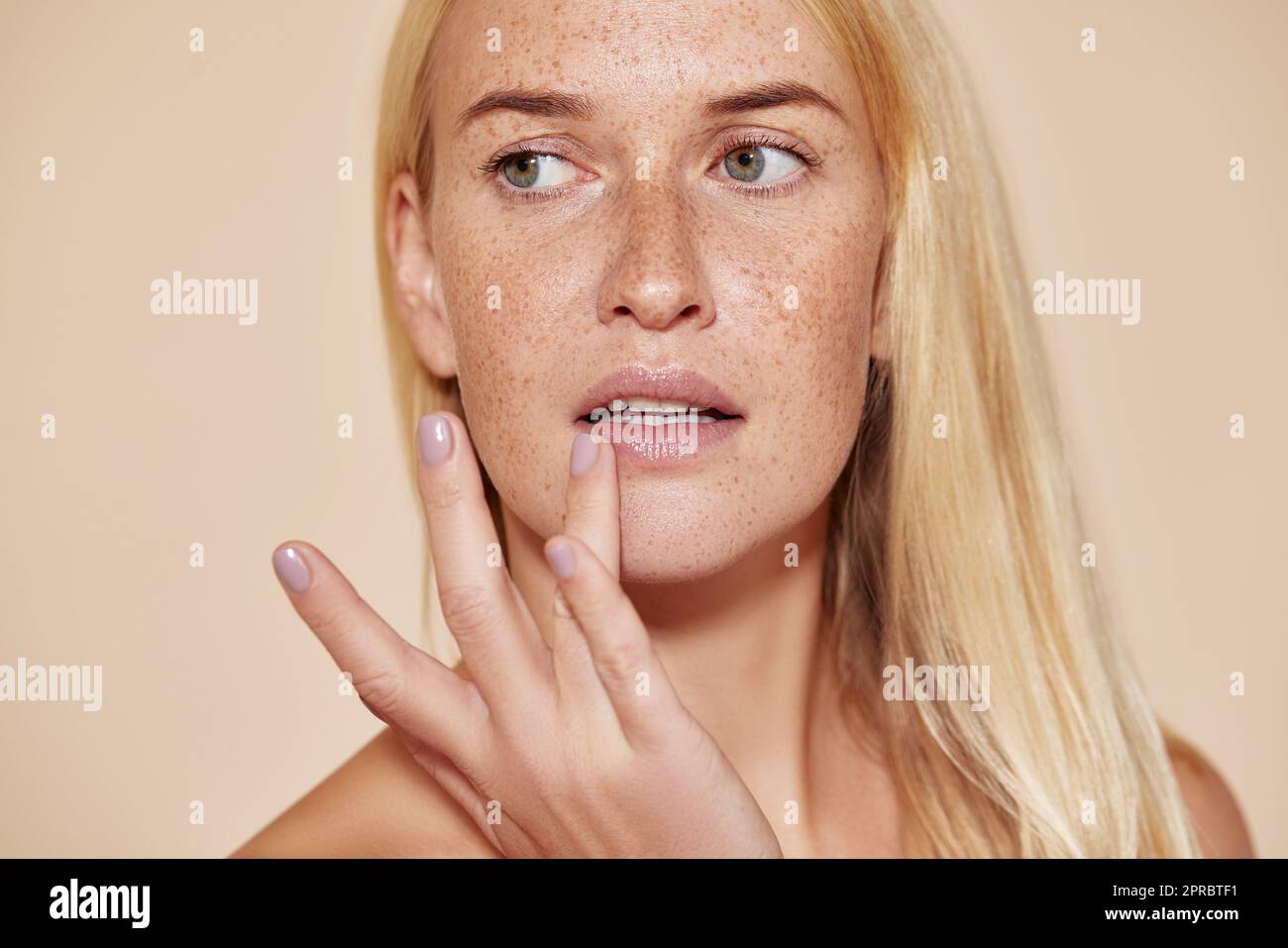 Eine Frau mit Sommersprossen, die ihre Lippe mit einem Finger berührt. Blonde Frau mit perfekter Haut, die Balsam auf die Lippen aufträgt. Stockfoto