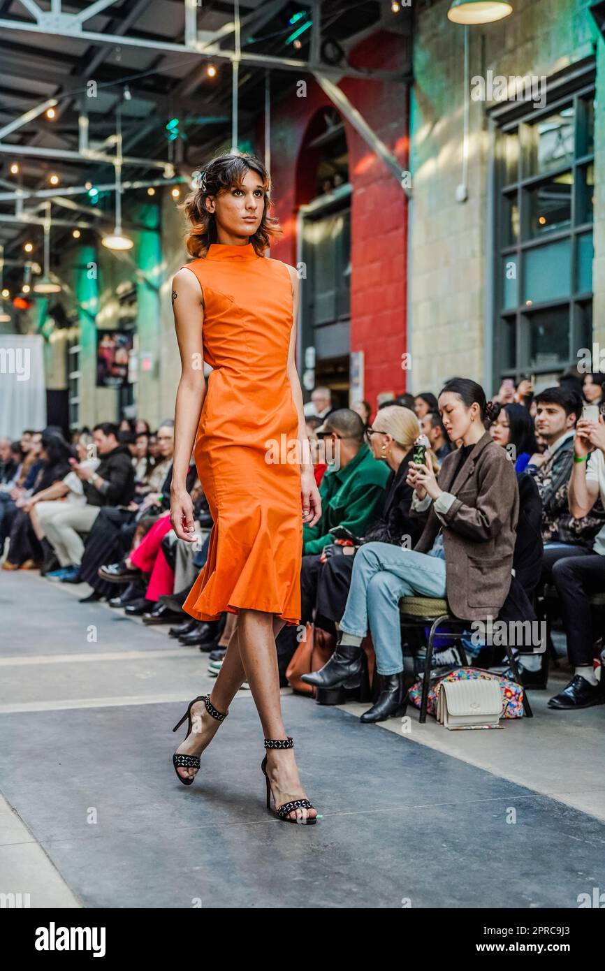 Männliches Kreuzkleid auf der Laufbahn als Model in einem orangefarbenen engen Kleid und offenen Fersen Stockfoto
