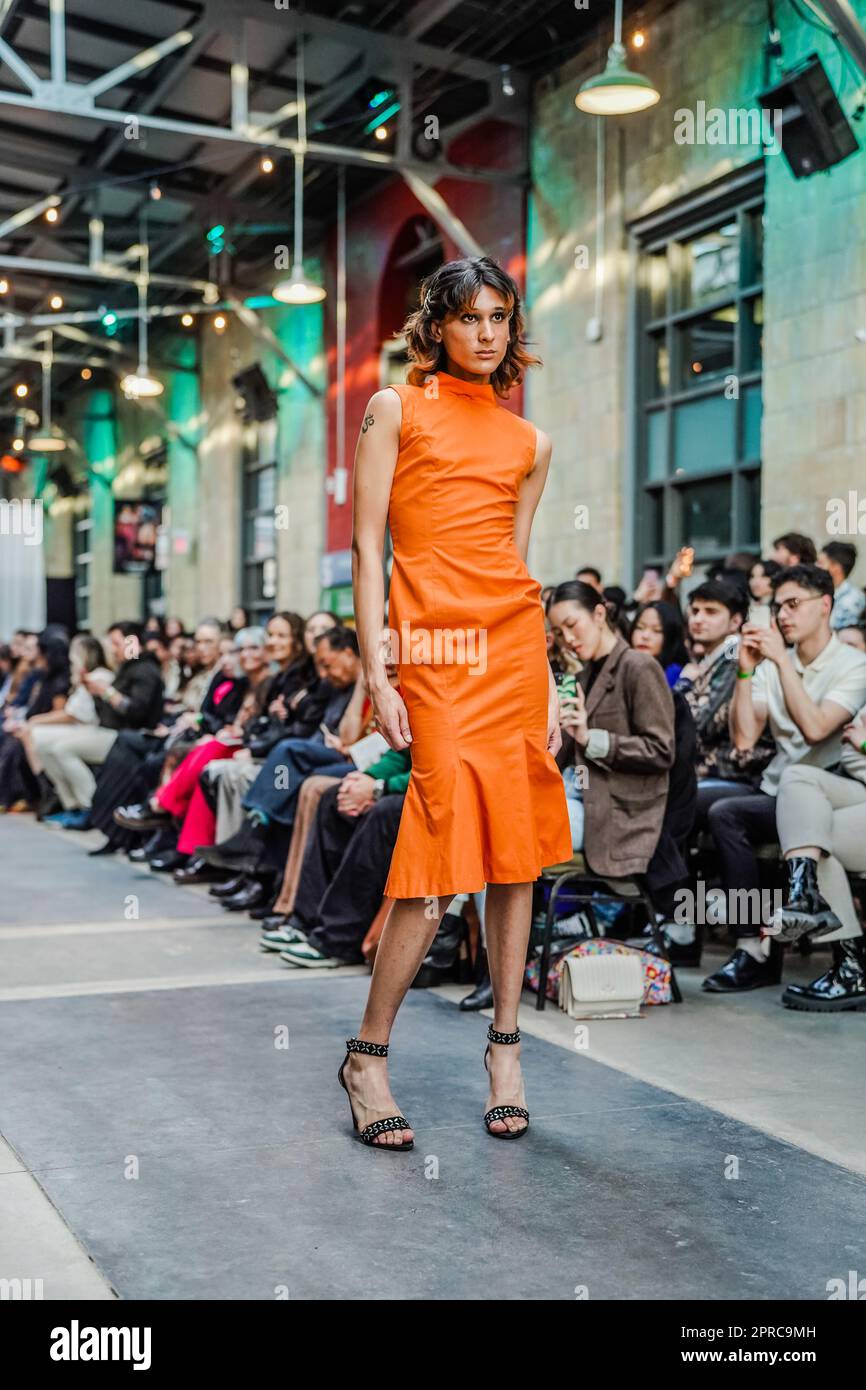 Männliches Kreuzkleid auf der Laufbahn als Model in einem orangefarbenen engen Kleid und offenen Fersen Stockfoto