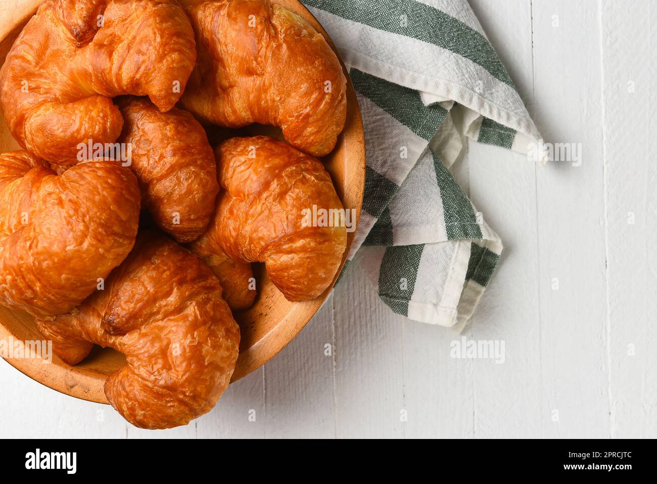 Eine Holzschüssel voller frisch gebackener Croissants auf einem Weißholztisch mit Küchenhandtuch. Stockfoto