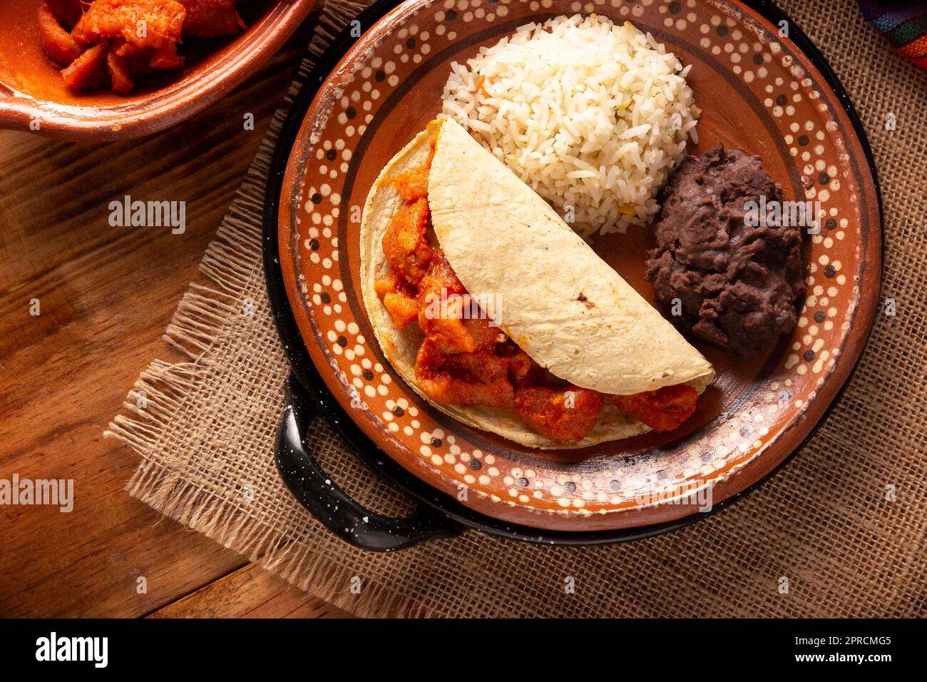 Schweineschinden in roter Soße Taco, dazu Reis und gekühlte Bohnen. Traditionelles hausgemachtes Gericht sehr beliebt in Mexiko, dieses Gericht ist Teil des beliebten Stockfoto