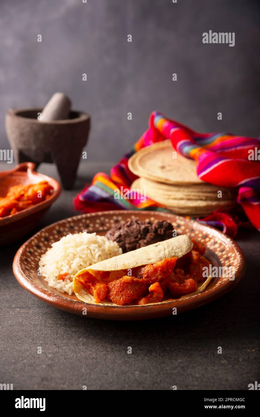 Schweineschinden in roter Soße Taco, dazu Reis und gekühlte Bohnen. Traditionelles hausgemachtes Gericht sehr beliebt in Mexiko, dieses Gericht ist Teil des beliebten Stockfoto