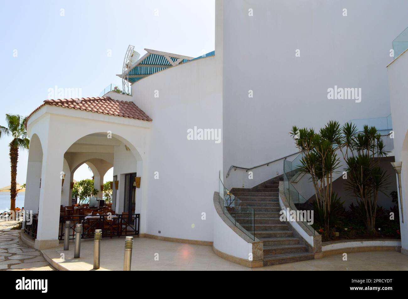 Ein großes stabiles weißes Betonsteingebäude mit einem Dach aus roten Fliesen in einem warmen tropischen exotischen südlichen Resort, das sich am blauen Meer von Palmen tr. Befindet Stockfoto