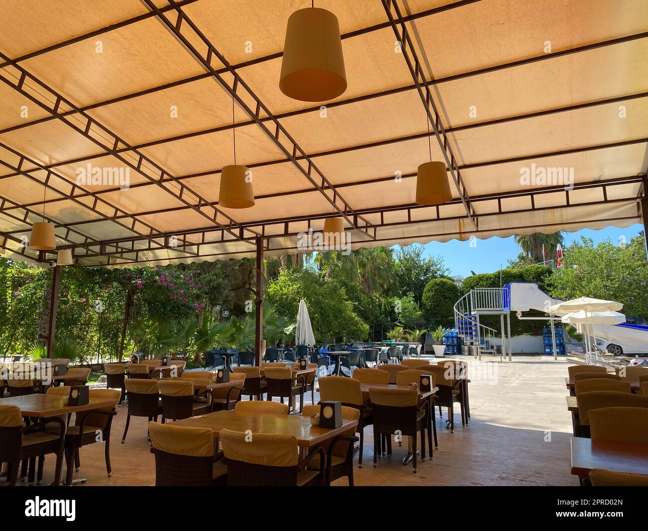 Ein offenes Cafe mit einem Bartisch mit Holztischen und -Stühlen auf der Straße mit einer offenen Veranda in einem tropischen warmen Land in einem Rest Resort mit Palmen tr Stockfoto