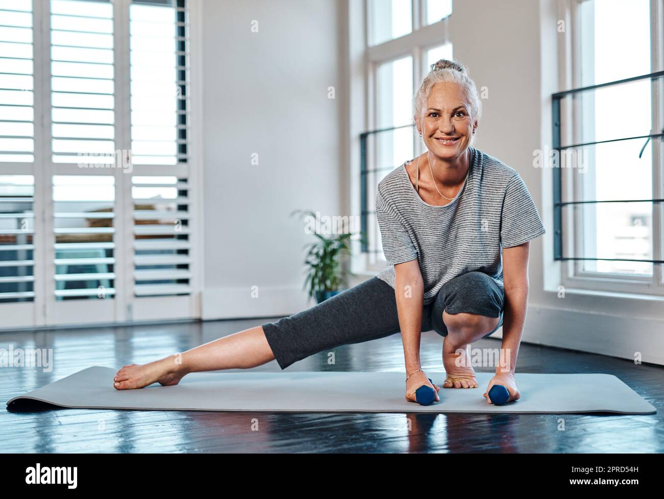 Kleine Gewichte neigen dazu, ein wenig zu helfen. Porträt einer fröhlichen reifen Frau, die tagsüber Yoga praktiziert und dabei Gewichte in einem Studio verwendet. Stockfoto
