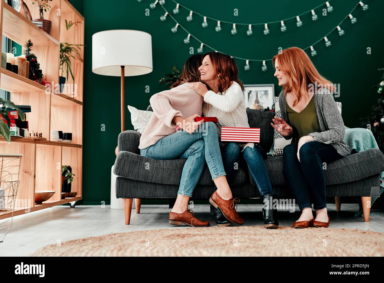 Sie sind die Besten. Drei attraktive Frauen mittleren Alters öffnen Geschenke zusammen, während sie während der Weihnachtszeit auf einem Sofa sitzen. Stockfoto