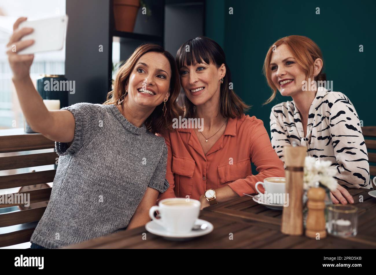 Immer noch Freunde und immer noch Fotos zusammen machen. Eine Gruppe attraktiver Frauen mittleren Alters, die ein Selbstporträt zusammen machen, während sie tagsüber in einem Café sitzen. Stockfoto