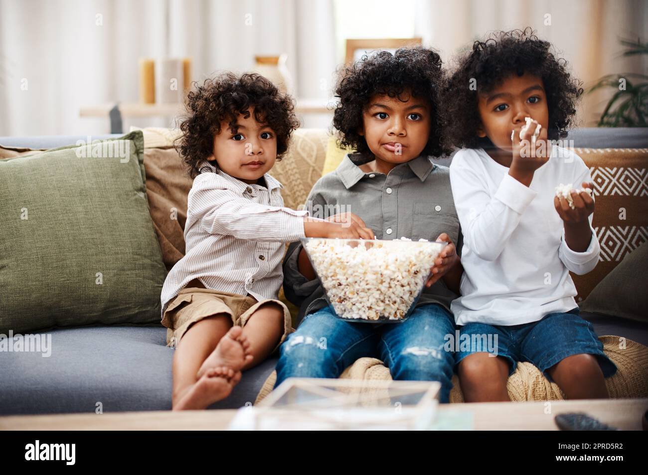 Jungs werden Jungen sein. Drei liebenswerte kleine Jungen essen Popcorn und schauen sich gemeinsam zu Hause Filme an. Stockfoto