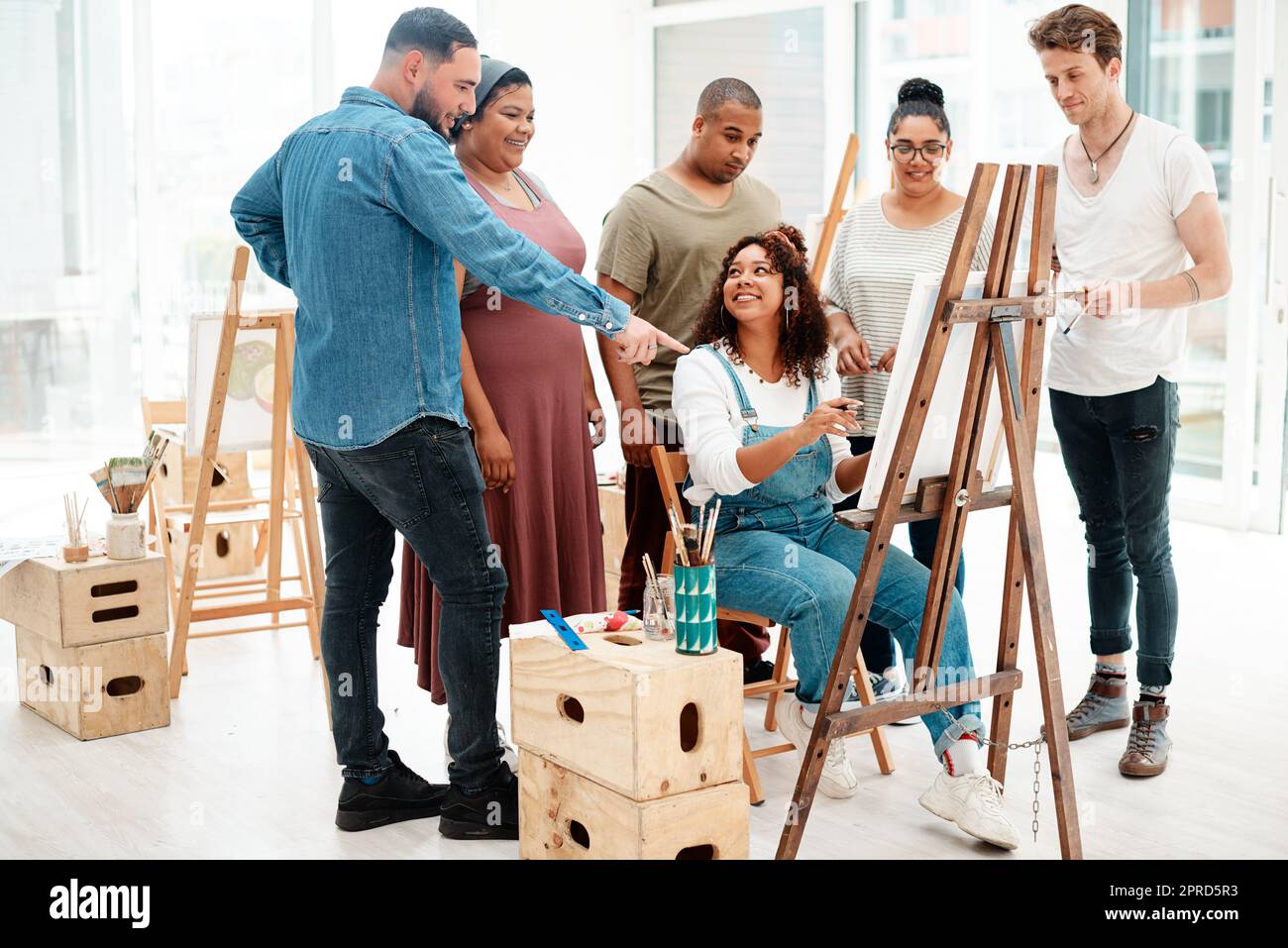 Mir gefällt, wie das aussieht. Ganzkörperaufnahme einer attraktiven jungen Frau, die während eines Kunstunterlasses sitzt und ihren Freunden ihre Kunstwerke erklärt. Stockfoto