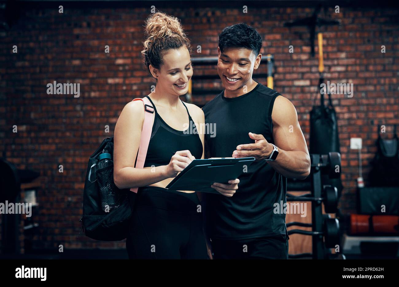 Melden Sie sich für unser neues Fitnessprogramm an. Eine sportliche junge Frau im Gespräch mit einem Fitnesstrainer im Fitnessstudio. Stockfoto