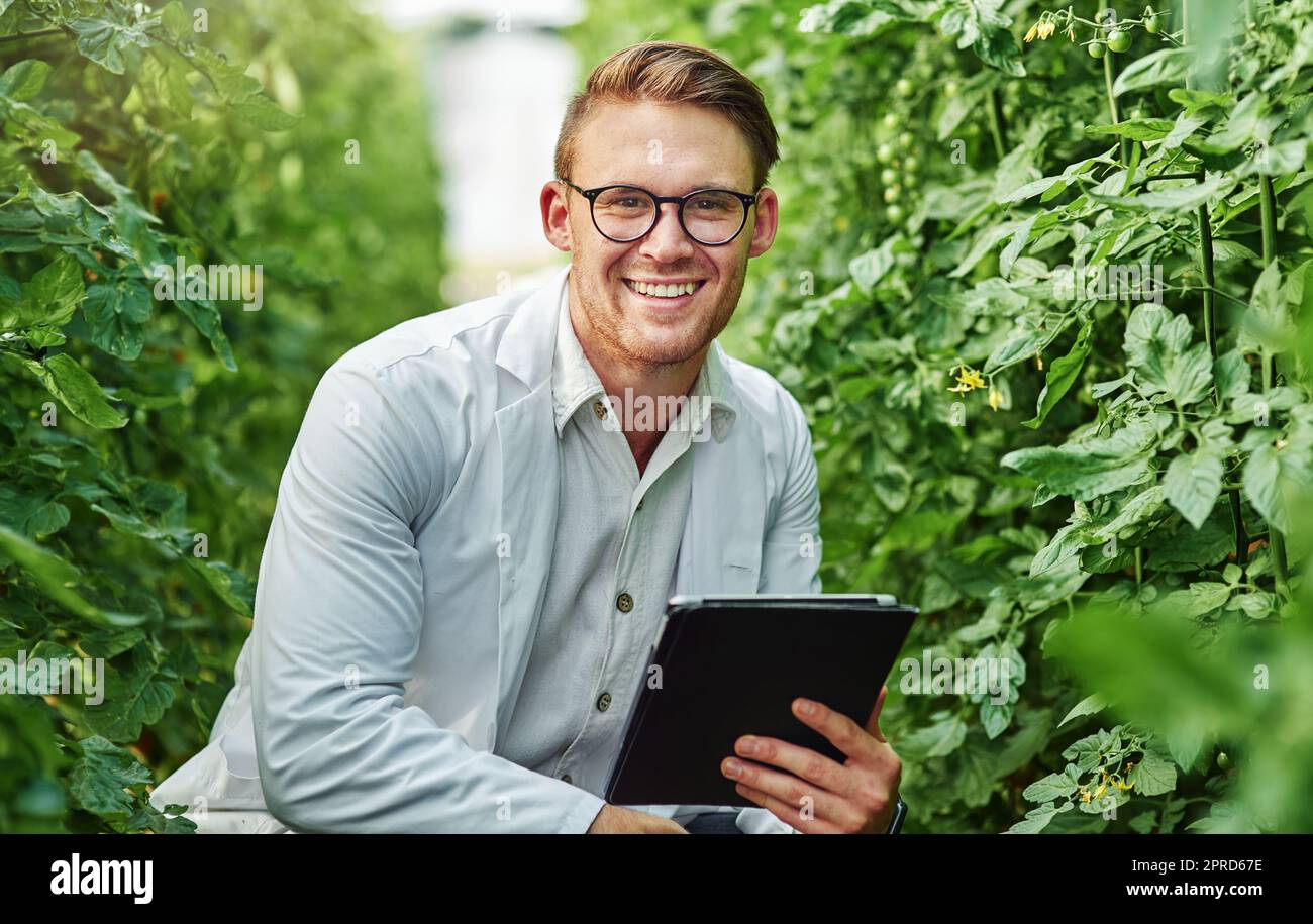 Ich liebe es einfach, draußen zu forschen. Porträt eines gutaussehenden jungen Wissenschaftlers, der ein digitales Tablet benutzt, während er Pflanzen und Kulturen im Freien auf einem Bauernhof studiert. Stockfoto