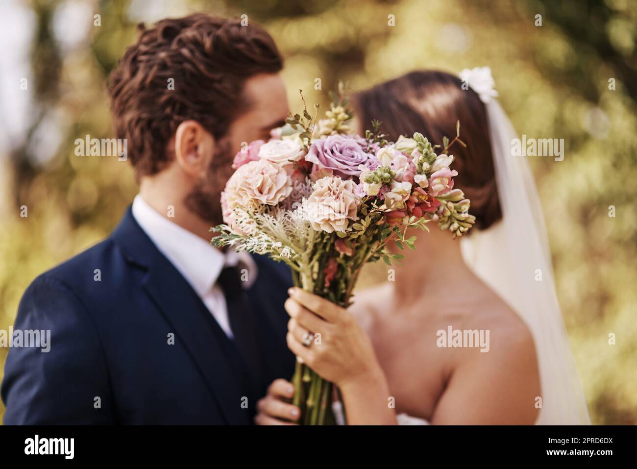 Ihre Liebe ist in voller Blüte. Ein unkenntlich frisch vermähltes Paar teilt einen intimen Moment, während sie draußen an ihrem Hochzeitstag steht. Stockfoto