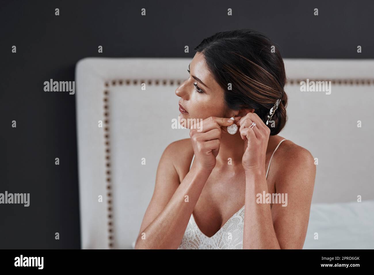 Es ist der große Tag. Eine attraktive junge Braut setzen in ihre Ohrringe, während sie sich für ihre Hochzeitszeremonie angezogen. Stockfoto