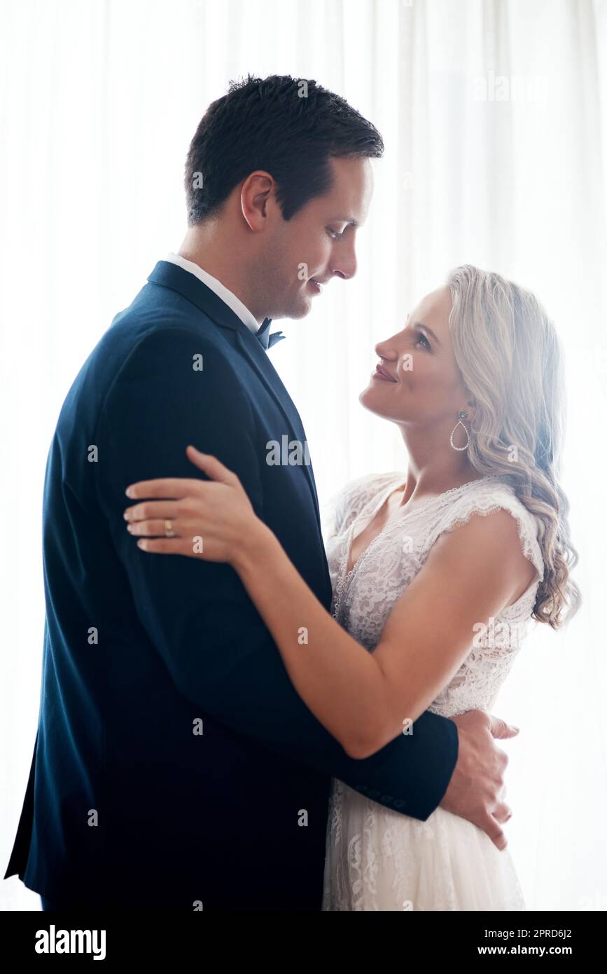 Heres zu neuen Anfängen. Ein glückliches junges Paar, das drinnen steht und sich nach ihrer Hochzeit liebevoll hält. Stockfoto