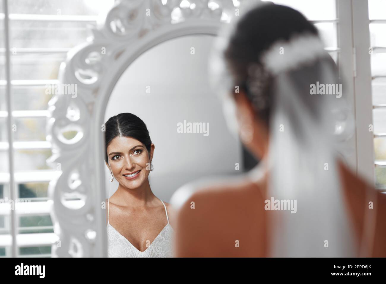 Also... der große Tag ist endlich da. Rückansicht einer attraktiven jungen Braut, die in den Spiegel schaut, während sie sich für ihre Hochzeitszeremonie vorbereitet. Stockfoto