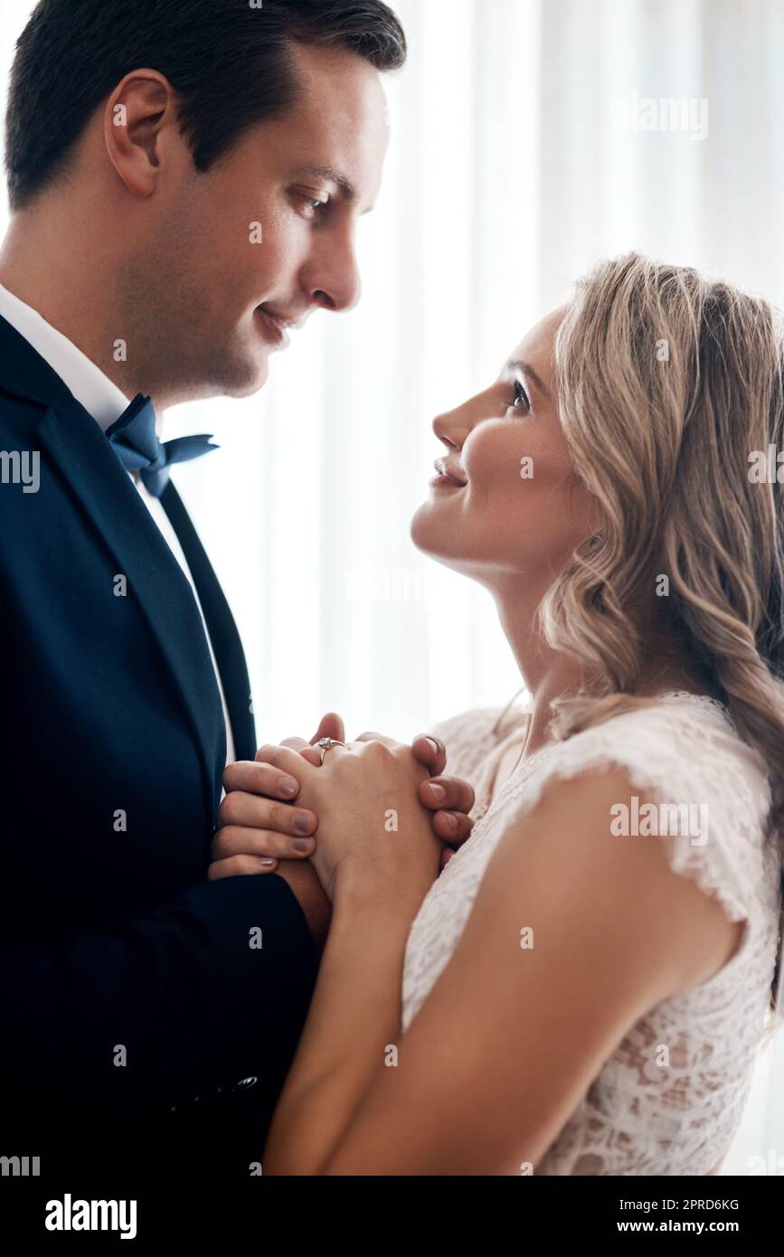 Ein glückliches junges Paar, das drinnen steht und sich nach ihrer Hochzeit liebevoll in der Hand hält. Stockfoto