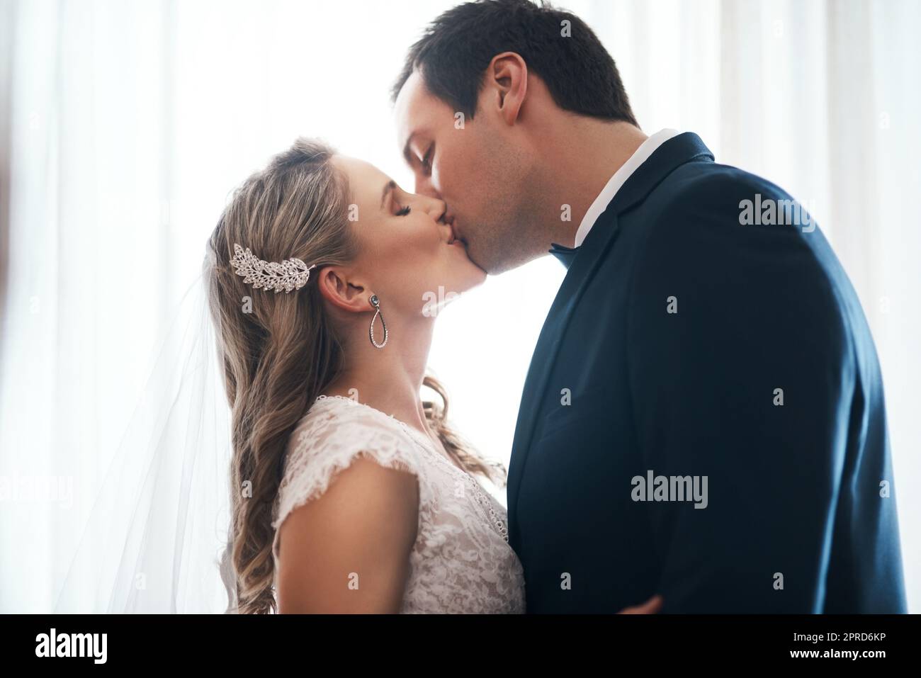 Versiegelt mit einem Kuss. Ein liebevolles junges Paar steht drinnen zusammen und küsst sich nach ihrer Hochzeit. Stockfoto