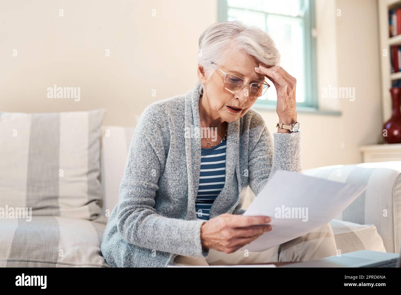 Ich kann mich diese Rückzahlungen nicht mehr leisten. Eine ältere Frau, die gestresst aussieht, während sie zu Hause Papierkram durchläuft. Stockfoto