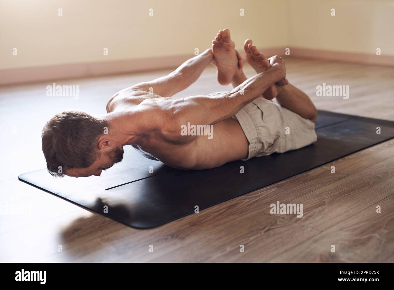 Yoga erfrischt Körper und Seele. Ganzkörperaufnahme eines flexiblen jungen Mannes, der sich in Innenräumen dehnt und Yoga praktiziert. Stockfoto